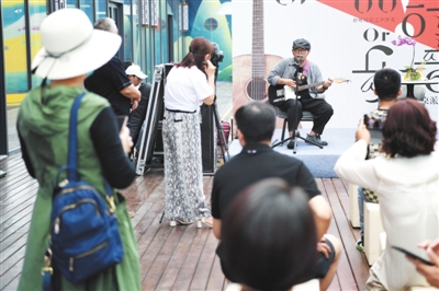 7月12日，在银川市金凤区唐徕公园西侧，歌手李晨阳献唱民谣，吸引众多市民围观。当日，银川市诗歌学会举办圆桌派第三期活动，邀请广大市民免费参加，以音乐和诗歌的形式，促进邻里感情。    本报记者  季正  摄